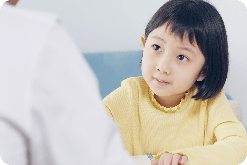 座りながら前にいる大人越しにその大人を見つめる女の子